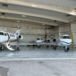 three private jets in an airport hanger, one jet preparing to board passengers
